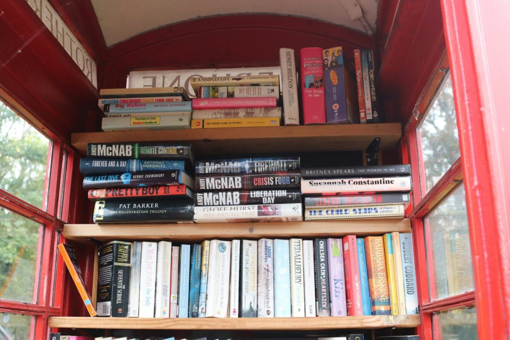 Books fill shelves inside a red telephone booth.